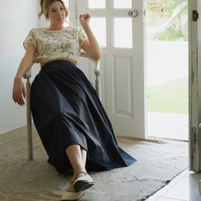 Woman sitting on a chair wearing a lace top and dark skirt in a bright room
