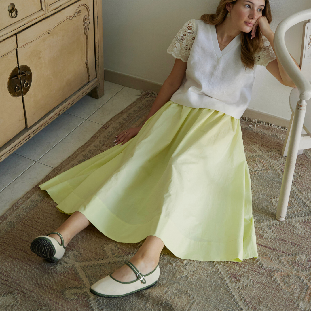 Woman sitting on a chair wearing a white top and yellow skirt in a room with wooden furniture